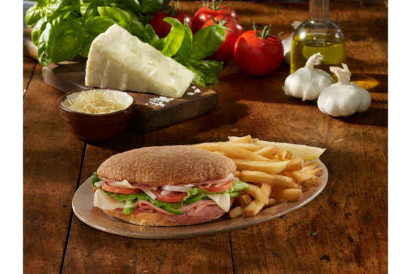 Italian ciabatta sandwich on the board with ham tomato lettuce and other toppings with a side of fries