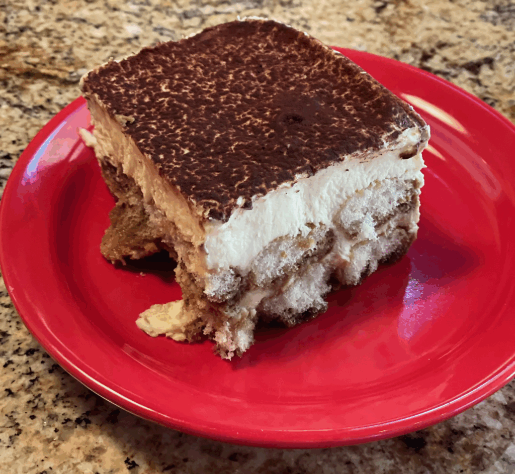 delicious tiramisu on a plate showing off the cocoa powder on top, cream, finger ladies, and chocolate throghout